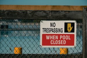 A 'No Trespassing' sign on a chain link fence at a closed swimming pool, ensurin