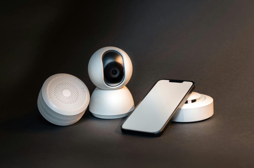 A sleek smartphone with modern smart home devices on a minimalist gray backgroun