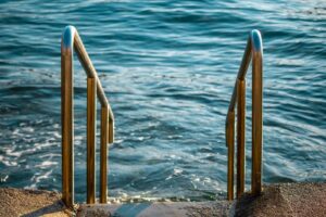 Close-up of stainless steel pool handrails leading to a calm ocean view.