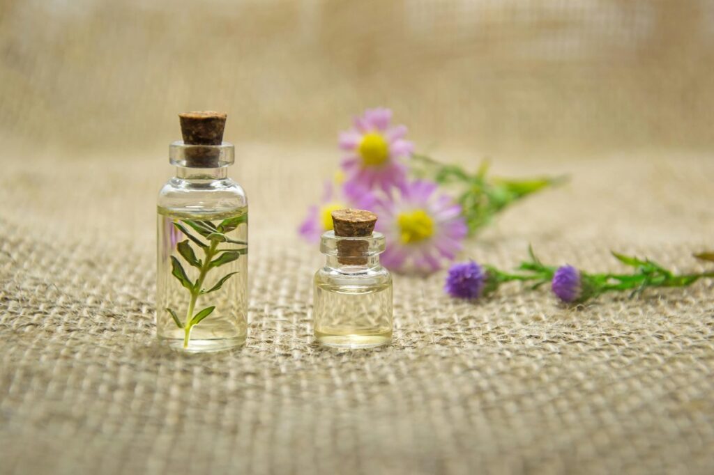 Glass bottles with essential oils and fresh flowers on burlap fabric creating a