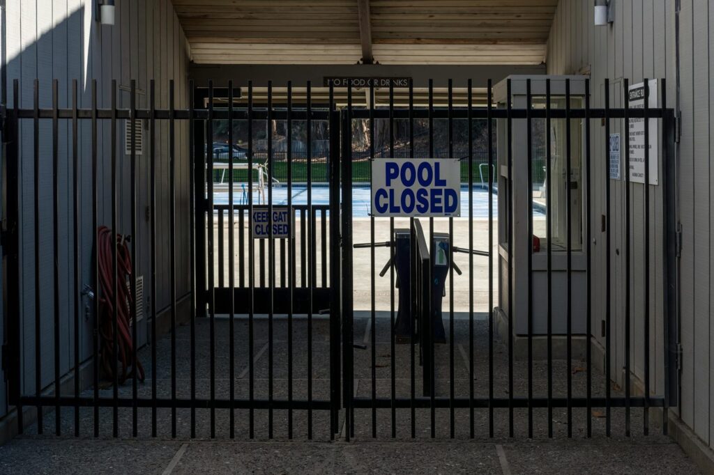 Iron gate blocking a closed community pool entrance with a clear sign.