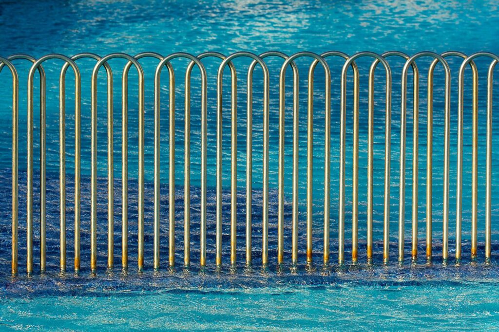 Modern metal fence with wave pattern beside a clear blue swimming pool, creating