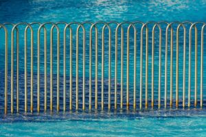 Modern metal fence with wave pattern beside a clear blue swimming pool, creating