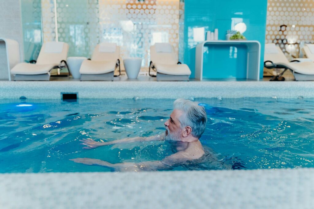 Older man enjoying a swim in a stylish indoor pool facility with relaxation chai