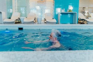 Older man enjoying a swim in a stylish indoor pool facility with relaxation chai