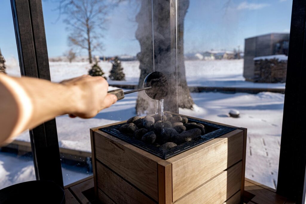 Steam rises from sauna stones as water is poured in a snowy Nordic setting, capt