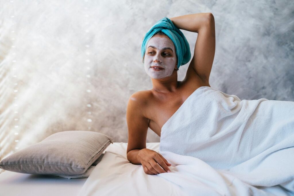 Woman enjoying a spa day with a facial mask and towel, embodying relaxation.