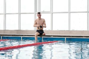 Young amputee athlete sitting by an indoor pool, preparing for swimming.